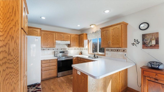 kitchen featuring electric range, freestanding refrigerator, a sink, a peninsula, and under cabinet range hood