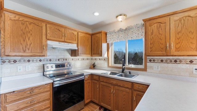 kitchen with under cabinet range hood, light countertops, a sink, and electric range