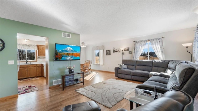 living area with light wood-type flooring, visible vents, and a textured ceiling