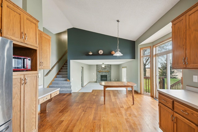 kitchen featuring open floor plan, light countertops, a large fireplace, light wood finished floors, and decorative light fixtures