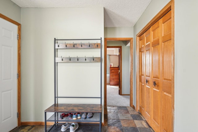mudroom with baseboards, stone finish flooring, and a textured ceiling