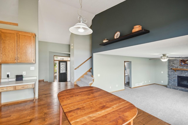 kitchen featuring ceiling fan, high vaulted ceiling, a stone fireplace, decorative light fixtures, and baseboards