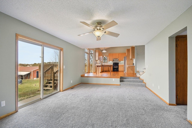 unfurnished living room featuring ceiling fan, light carpet, a textured ceiling, stairs, and baseboards