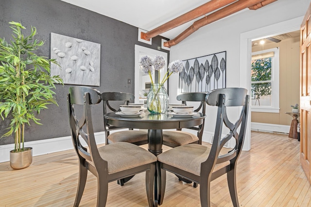 dining space with lofted ceiling with beams and light wood-type flooring