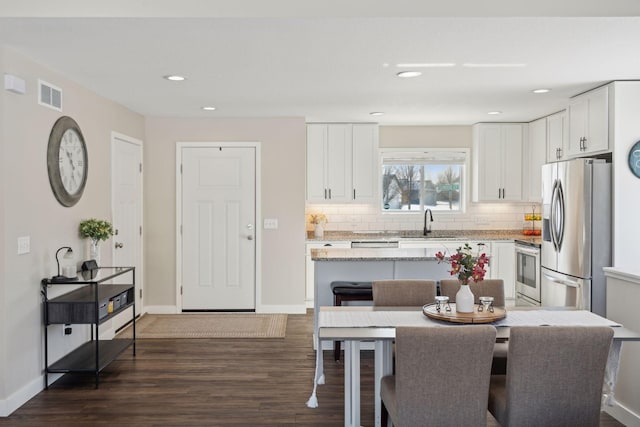 kitchen featuring white cabinets, decorative backsplash, light stone counters, stainless steel appliances, and a sink