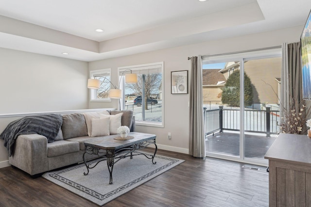 living room featuring dark wood-type flooring, a tray ceiling, plenty of natural light, and baseboards