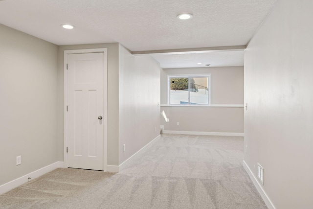 empty room featuring visible vents, light colored carpet, a textured ceiling, and baseboards