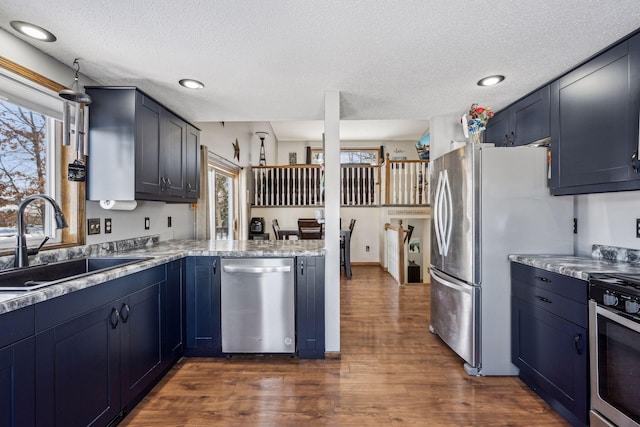 kitchen featuring appliances with stainless steel finishes, sink, dark hardwood / wood-style flooring, light stone counters, and kitchen peninsula