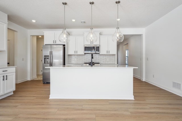 kitchen with white cabinetry, decorative light fixtures, stainless steel appliances, and an island with sink