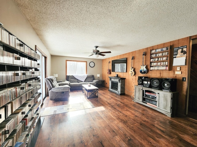 living room with ceiling fan, wooden walls, a textured ceiling, and dark hardwood / wood-style flooring