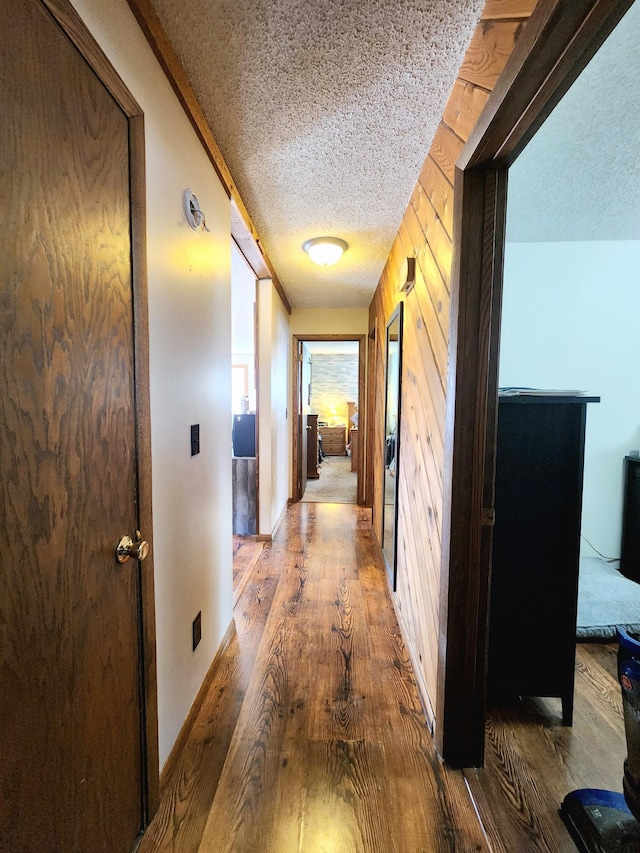 hallway with wood-type flooring, a textured ceiling, and wood walls