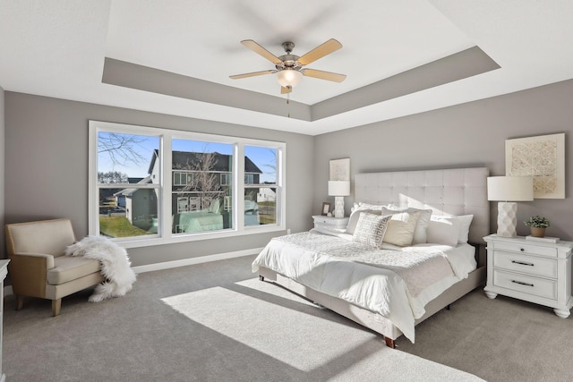 carpeted bedroom with a raised ceiling and ceiling fan