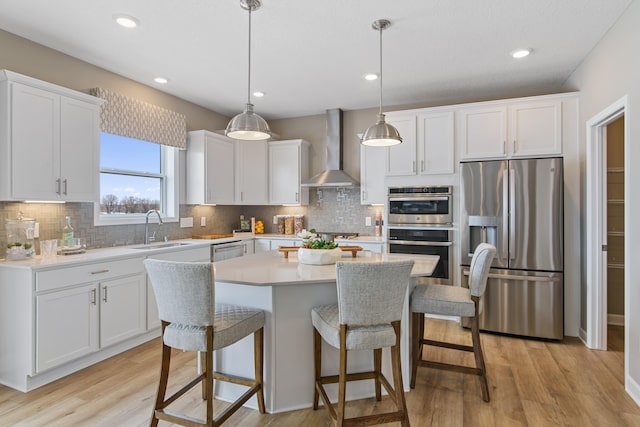 kitchen featuring wall chimney exhaust hood, white cabinetry, stainless steel appliances, and decorative light fixtures