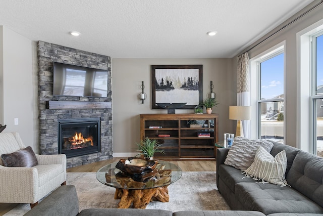 living room featuring wood-type flooring, a stone fireplace, and a textured ceiling