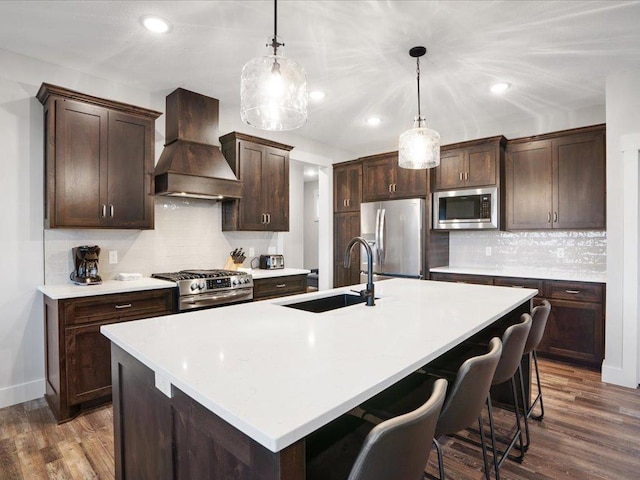 kitchen featuring custom exhaust hood, an island with sink, hanging light fixtures, and stainless steel appliances