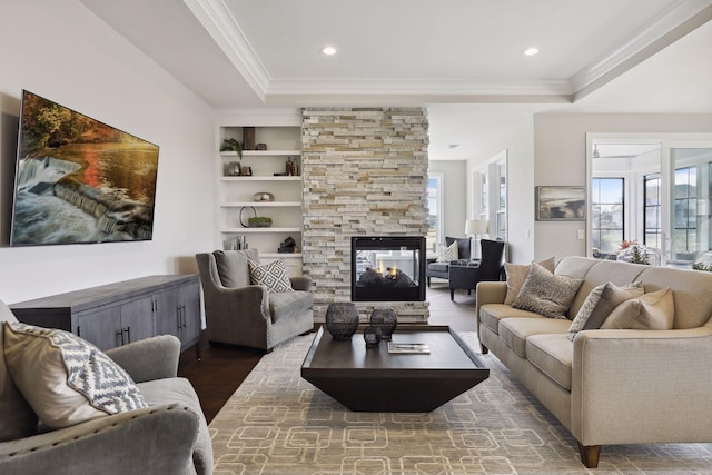 living room with built in shelves, plenty of natural light, ornamental molding, and a stone fireplace