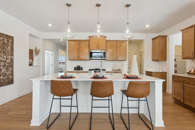 kitchen with pendant lighting, backsplash, a kitchen breakfast bar, and an island with sink