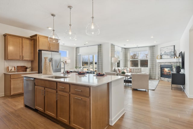 kitchen featuring stainless steel appliances, an island with sink, sink, and light hardwood / wood-style flooring