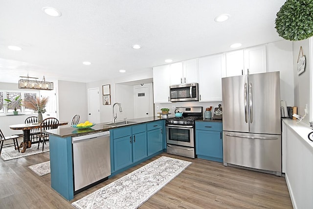 kitchen with stainless steel appliances, dark countertops, a sink, and blue cabinets