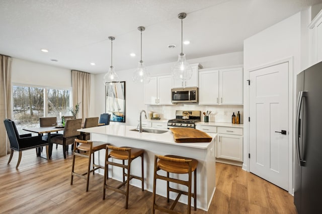 kitchen featuring sink, white cabinetry, appliances with stainless steel finishes, pendant lighting, and a kitchen island with sink