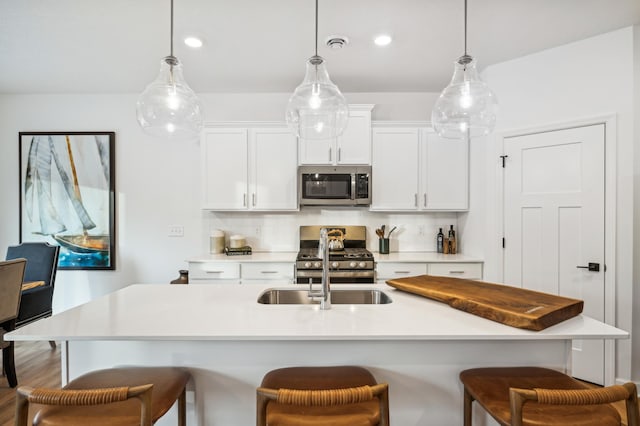 kitchen featuring pendant lighting, white cabinetry, appliances with stainless steel finishes, and a center island with sink