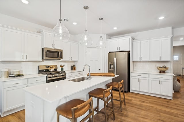 kitchen featuring pendant lighting, sink, appliances with stainless steel finishes, white cabinets, and a center island with sink