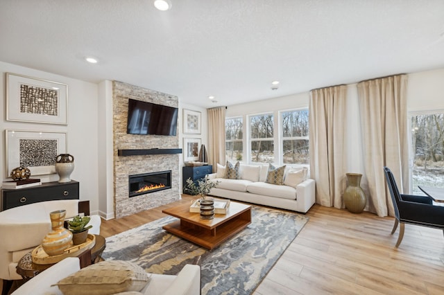 living room with plenty of natural light, a stone fireplace, light hardwood / wood-style flooring, and a textured ceiling