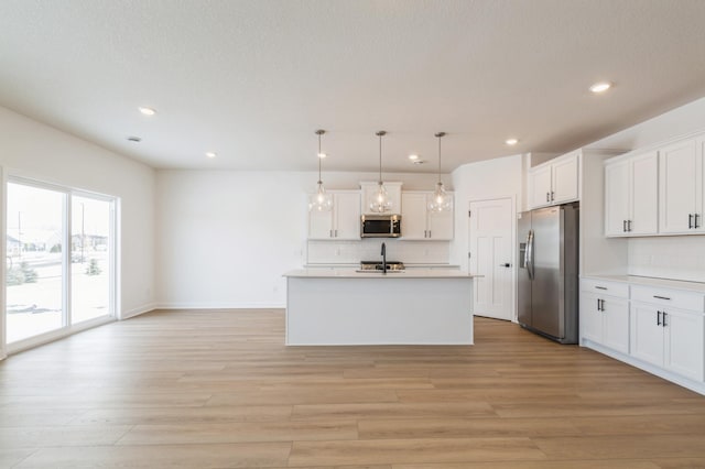 kitchen featuring white cabinetry, hanging light fixtures, an island with sink, stainless steel appliances, and light hardwood / wood-style floors