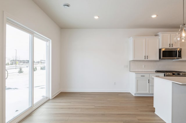 kitchen featuring pendant lighting, white cabinetry, backsplash, stainless steel appliances, and light wood-type flooring