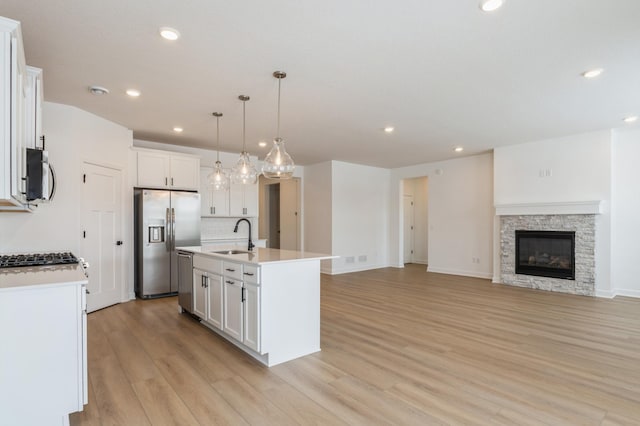 kitchen with pendant lighting, sink, a kitchen island with sink, stainless steel appliances, and white cabinets