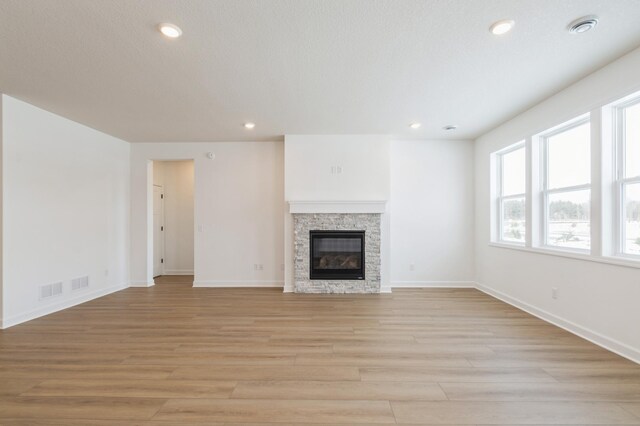 unfurnished living room featuring a stone fireplace, a textured ceiling, and light hardwood / wood-style flooring