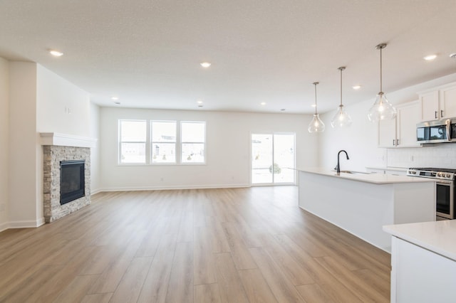 kitchen with pendant lighting, sink, appliances with stainless steel finishes, a kitchen island with sink, and white cabinets