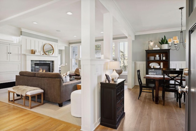 living room with a tiled fireplace, ornamental molding, light wood-type flooring, and wainscoting