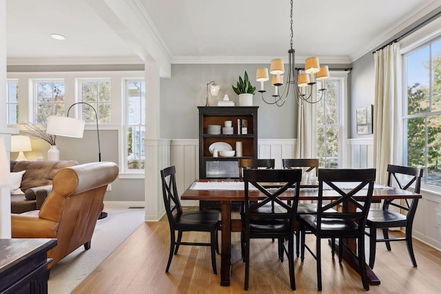 dining room featuring visible vents, crown molding, a chandelier, a wainscoted wall, and light wood-type flooring