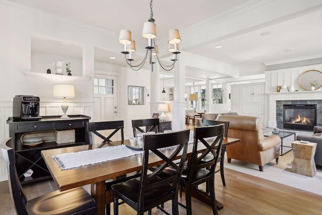 dining space featuring ornamental molding, wainscoting, a tile fireplace, wood finished floors, and a decorative wall