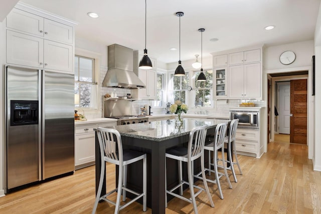 kitchen featuring light wood-style flooring, wall chimney exhaust hood, built in appliances, and a sink