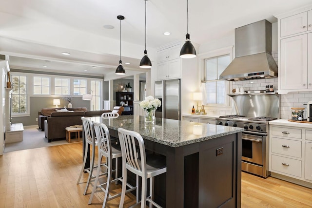 kitchen featuring plenty of natural light, a kitchen island, backsplash, appliances with stainless steel finishes, and wall chimney exhaust hood