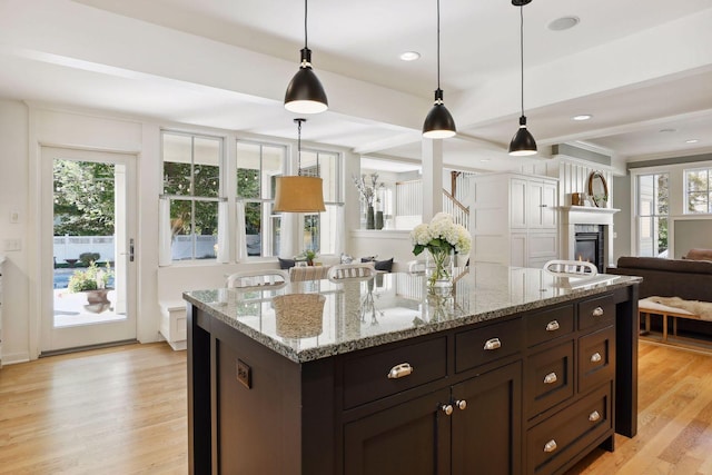 kitchen featuring a glass covered fireplace, light wood-style floors, pendant lighting, and open floor plan