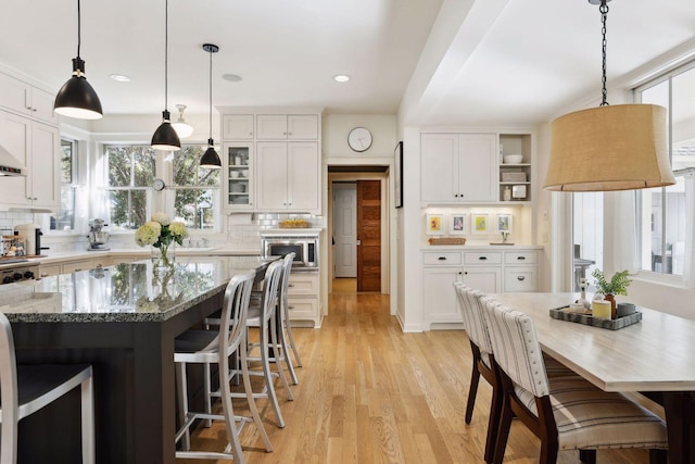 kitchen with stainless steel microwave, decorative backsplash, a kitchen breakfast bar, light wood-style floors, and white cabinets