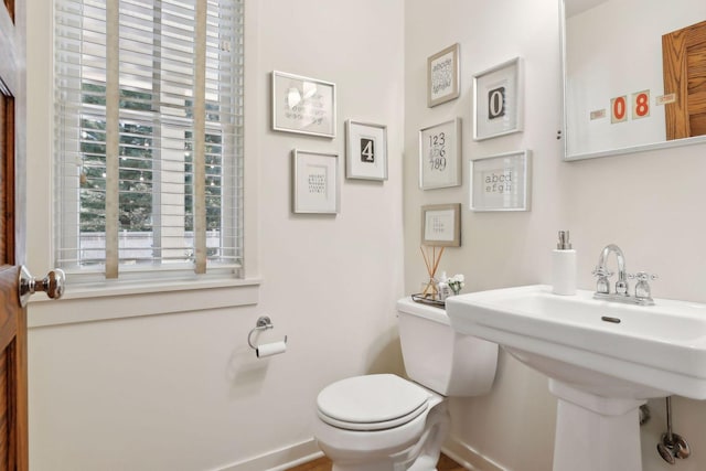 half bath with toilet, baseboards, and a sink