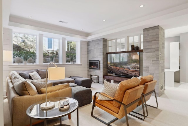 living room featuring visible vents, a tray ceiling, recessed lighting, a glass covered fireplace, and light colored carpet