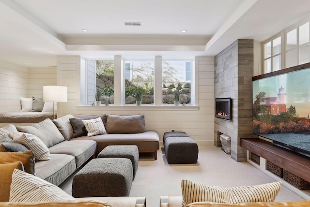 carpeted living area featuring wooden walls, a healthy amount of sunlight, visible vents, and a tile fireplace