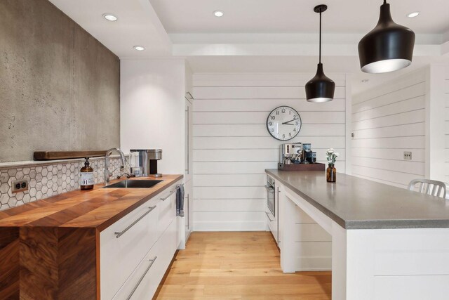 kitchen featuring decorative backsplash, light wood-style flooring, a peninsula, white cabinets, and a sink