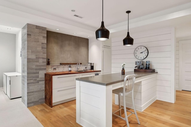 kitchen featuring a sink, a kitchen bar, light wood-type flooring, white cabinetry, and modern cabinets