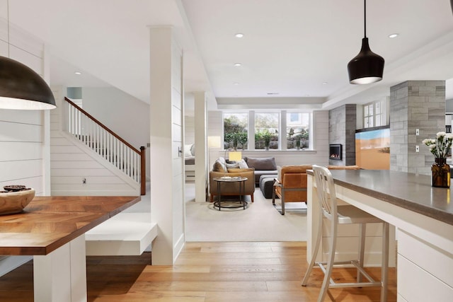 interior space featuring recessed lighting, light wood-type flooring, a warm lit fireplace, and stairs