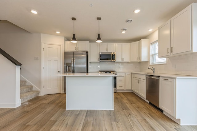 kitchen featuring appliances with stainless steel finishes, light hardwood / wood-style flooring, hanging light fixtures, and white cabinets