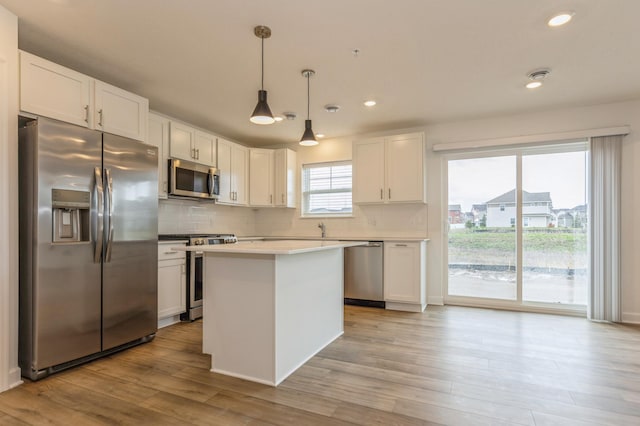 kitchen with appliances with stainless steel finishes, decorative light fixtures, white cabinetry, decorative backsplash, and light hardwood / wood-style flooring