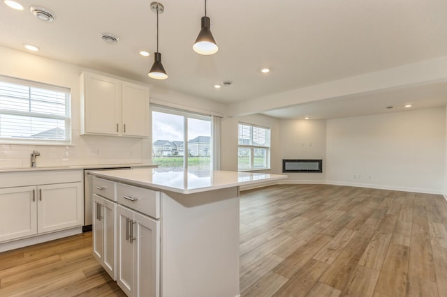 kitchen with sink, light wood-type flooring, pendant lighting, decorative backsplash, and white cabinets