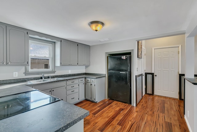 kitchen with gray cabinets, hardwood / wood-style floors, sink, stove, and black fridge