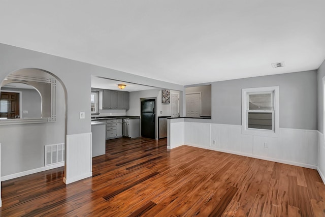 unfurnished living room featuring dark wood-style floors, visible vents, and wainscoting